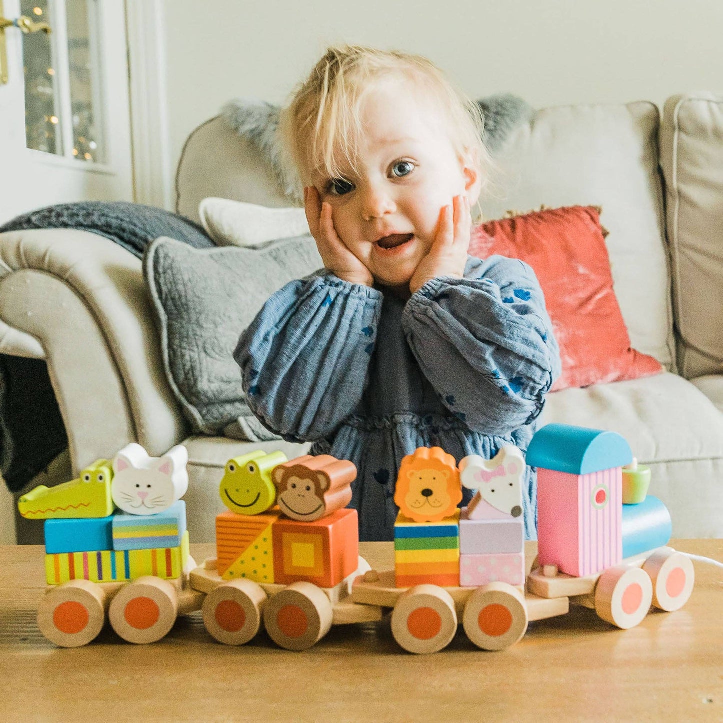 Child enjoying playing with a colourful wooden toy train on a wooden floor.