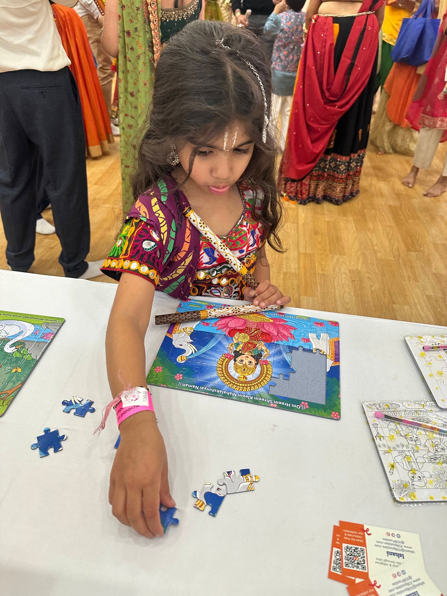 little girl holding dandiya sticks and playing with the lakshmi jigsaw puzzle at garba in harrow