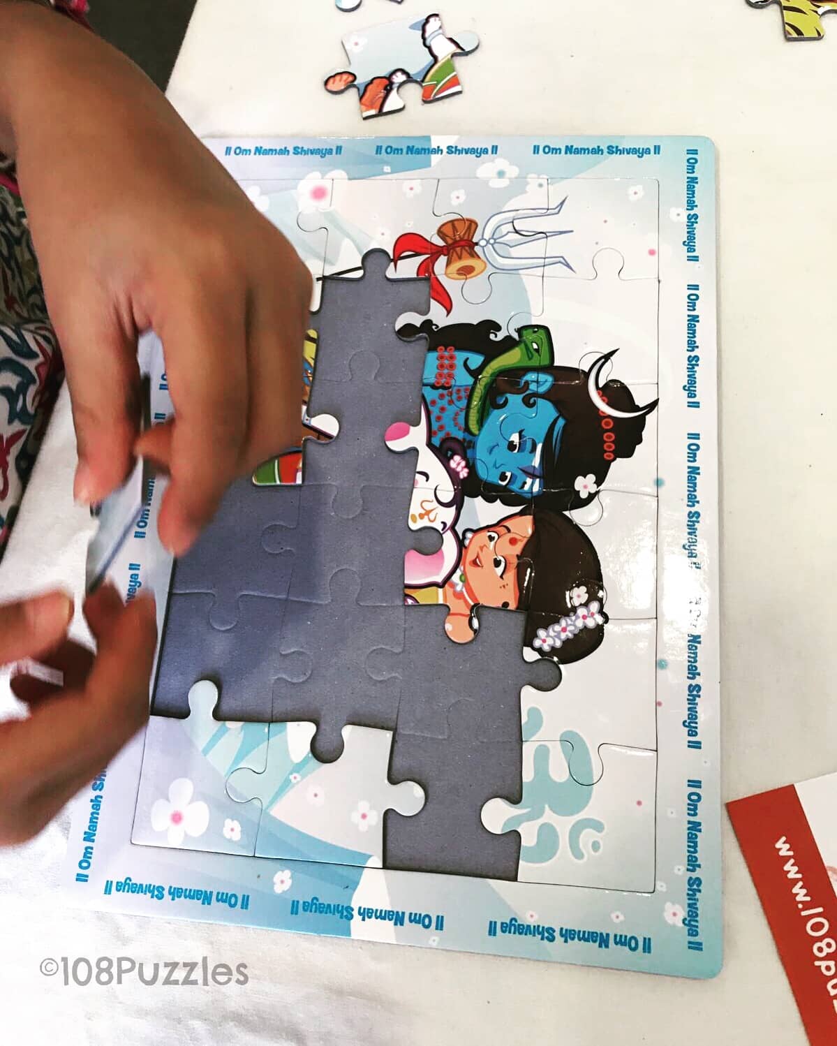 Child's hand placing a puzzle piece into the tray of a Hindu God puzzle