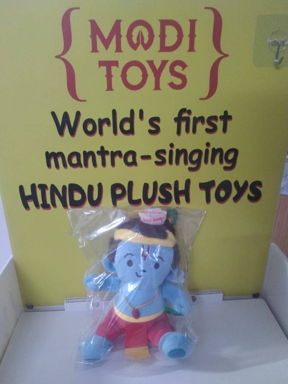 Plush toy in packaging with 'Modi Toys' sign claiming to be 'World's first mantra-singing Hindu plush toys'.