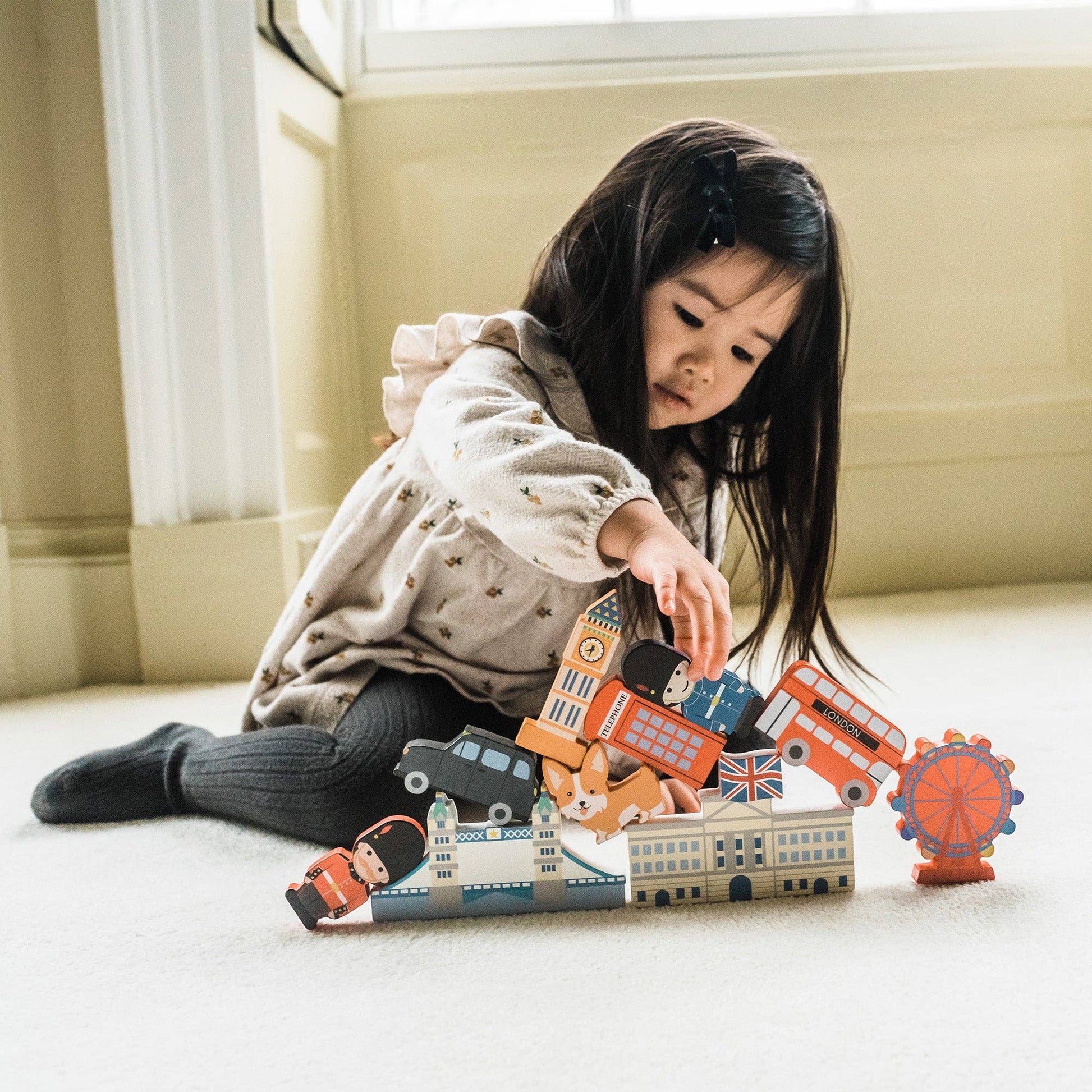 Child playing with London city blocks on a light-coloured floor.