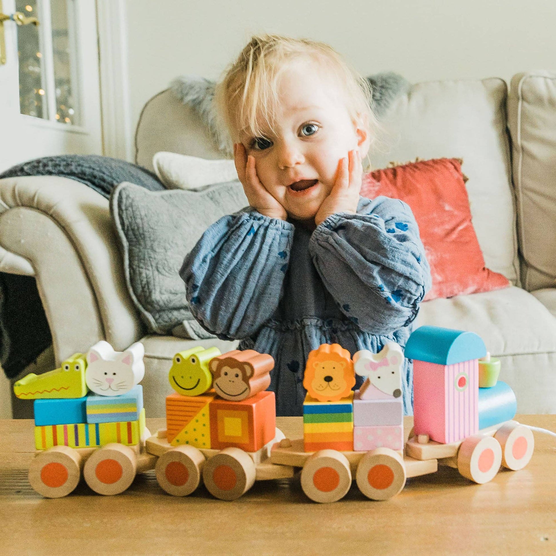 Child enjoying playing with a colourful wooden toy train on a wooden floor.