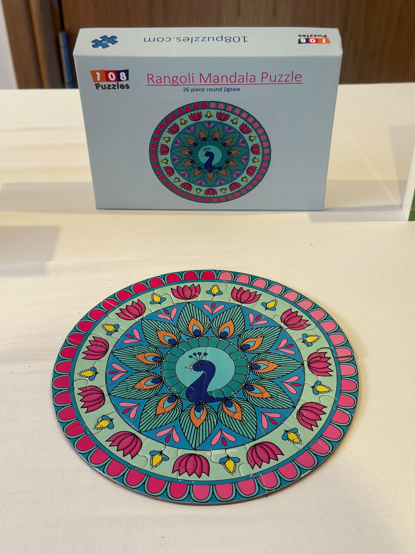 Colorful mandala puzzle on a white surface with a box labeled 'Rangoli Mandala Puzzle' in the background.
