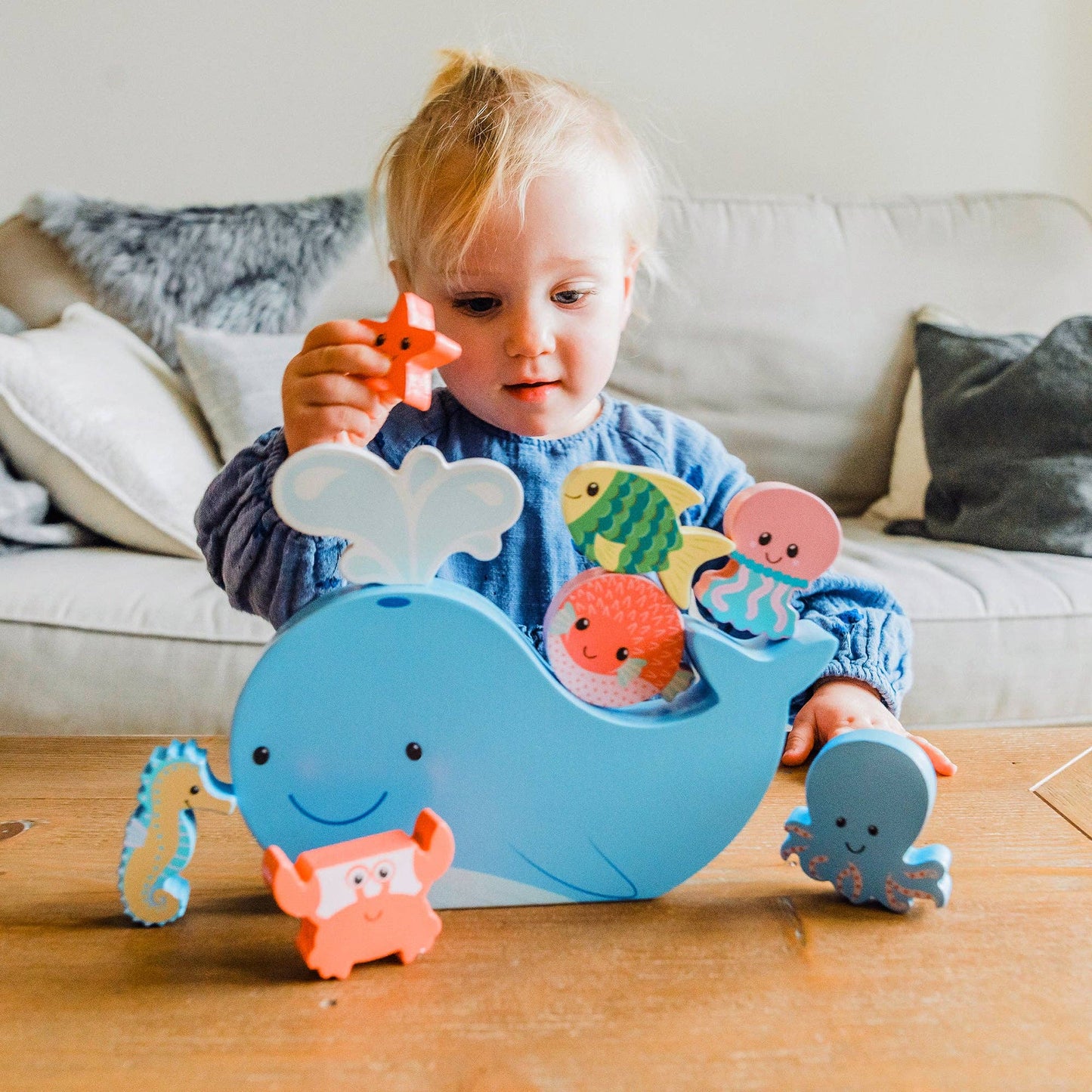 Child playing with a toy whale and sea creatures on a wooden floor.