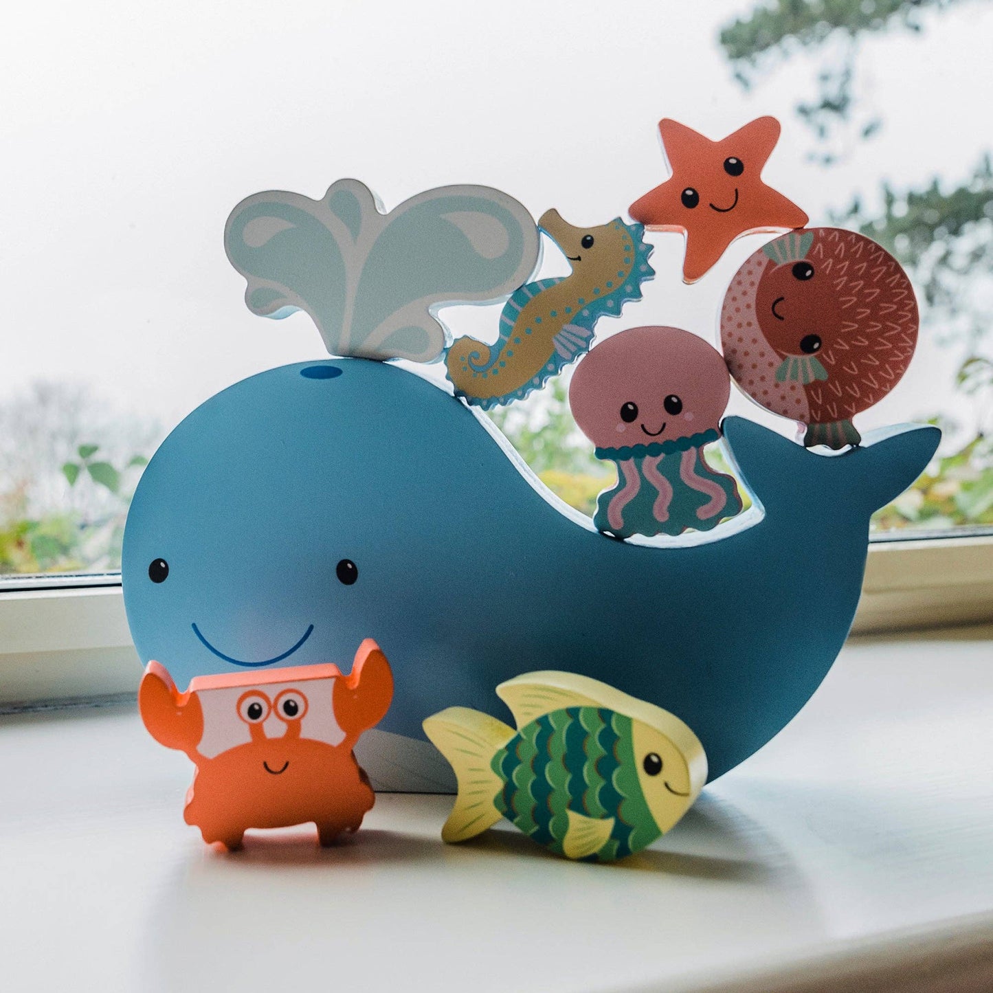 Colourful wooden toy whale with various sea creature figures balancing on top sitting on a windowsill